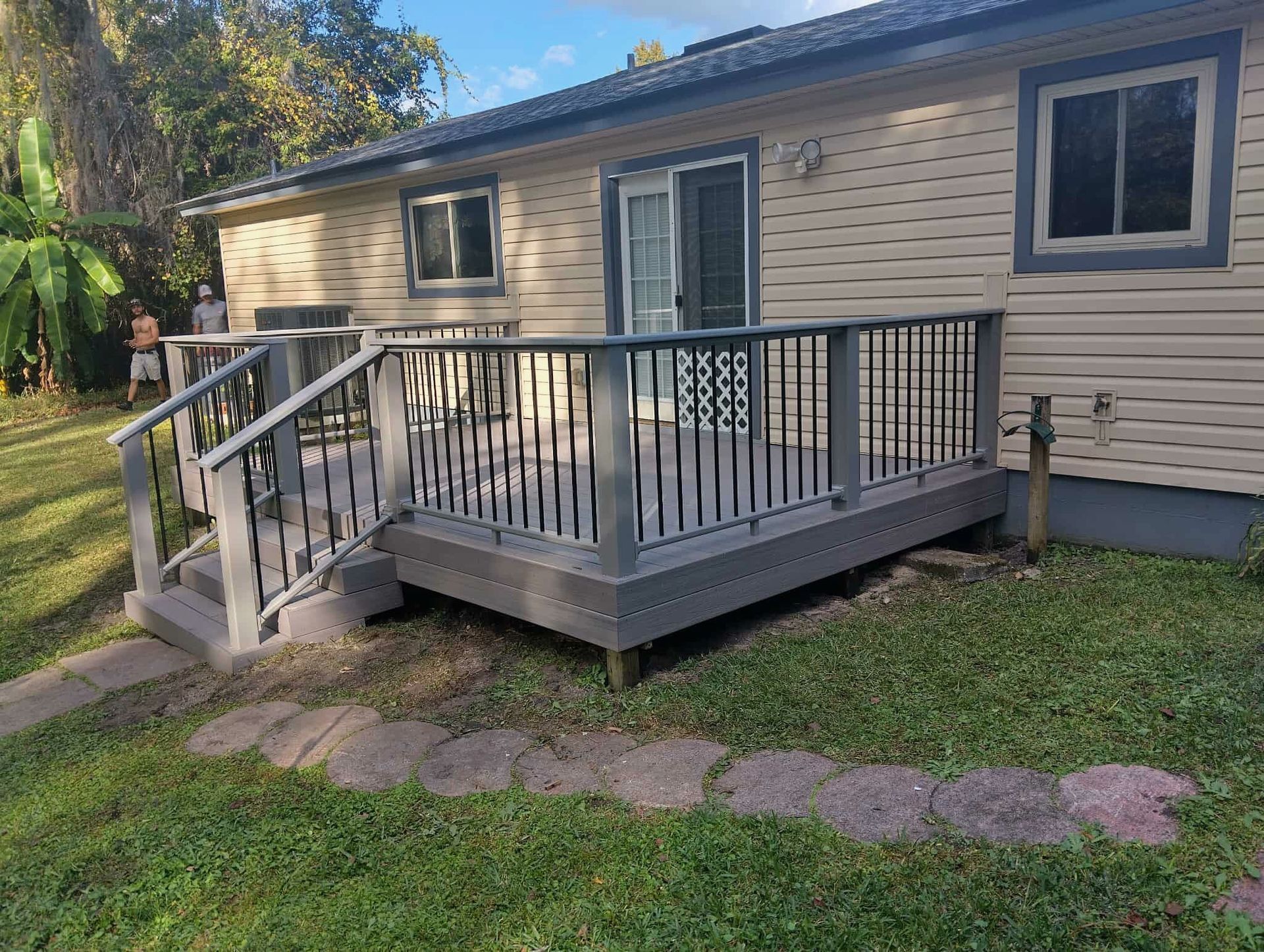 Small wooden front deck with black railings on a beige house, viewed from the yard.