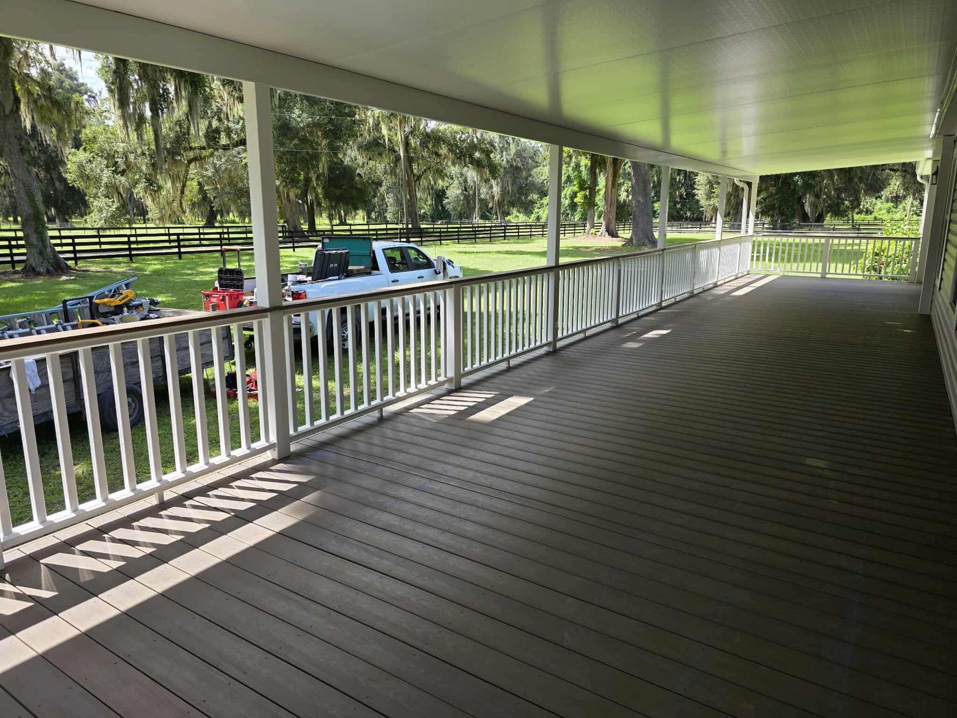 Covered wooden porch with white railings overlooking a tree-lined street and parked cars