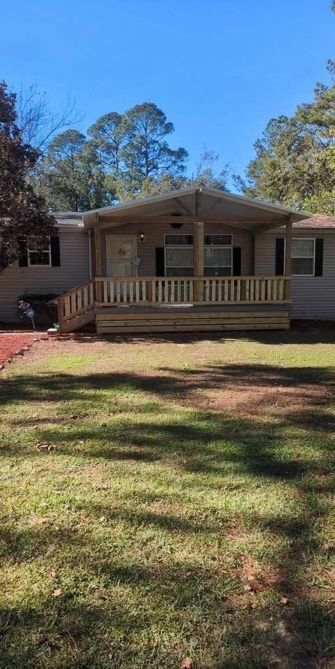 Single-story beige house with a front porch and ramp, set behind a grassy yard and trees.