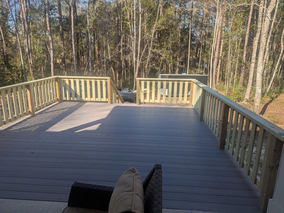 Wooden deck overlooking a wooded area with railings and a small opening at the far end