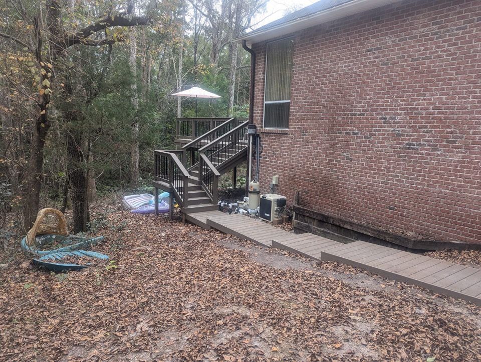 Backyard with brick house, wooden stairs, leaf-covered ground, and a patio umbrella among trees