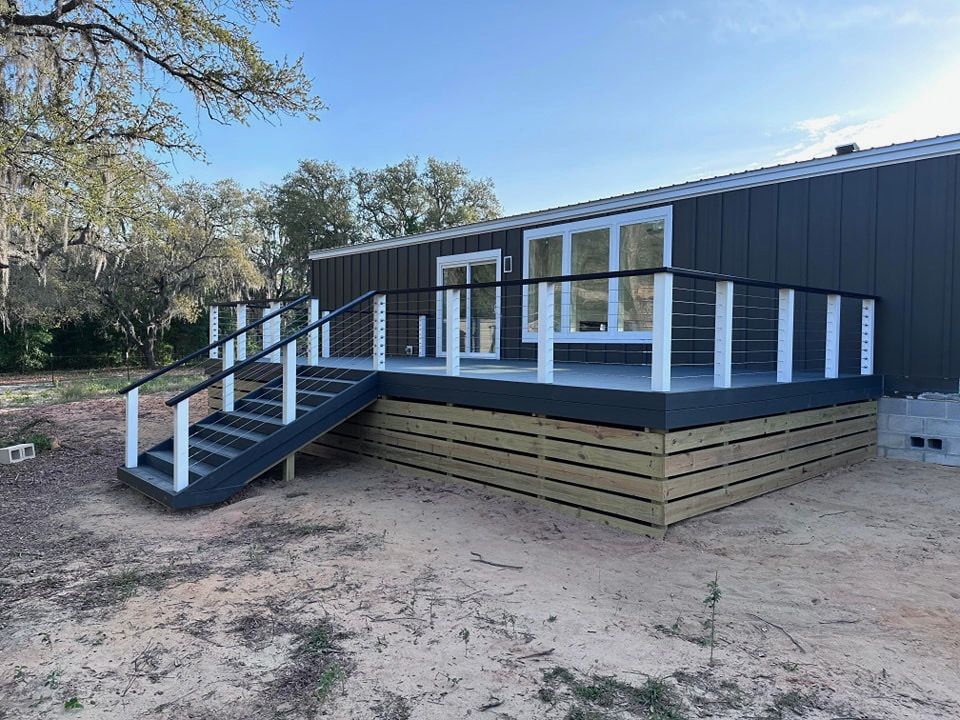 Modular dark gray building with white railings and front stairs on a dirt lot
