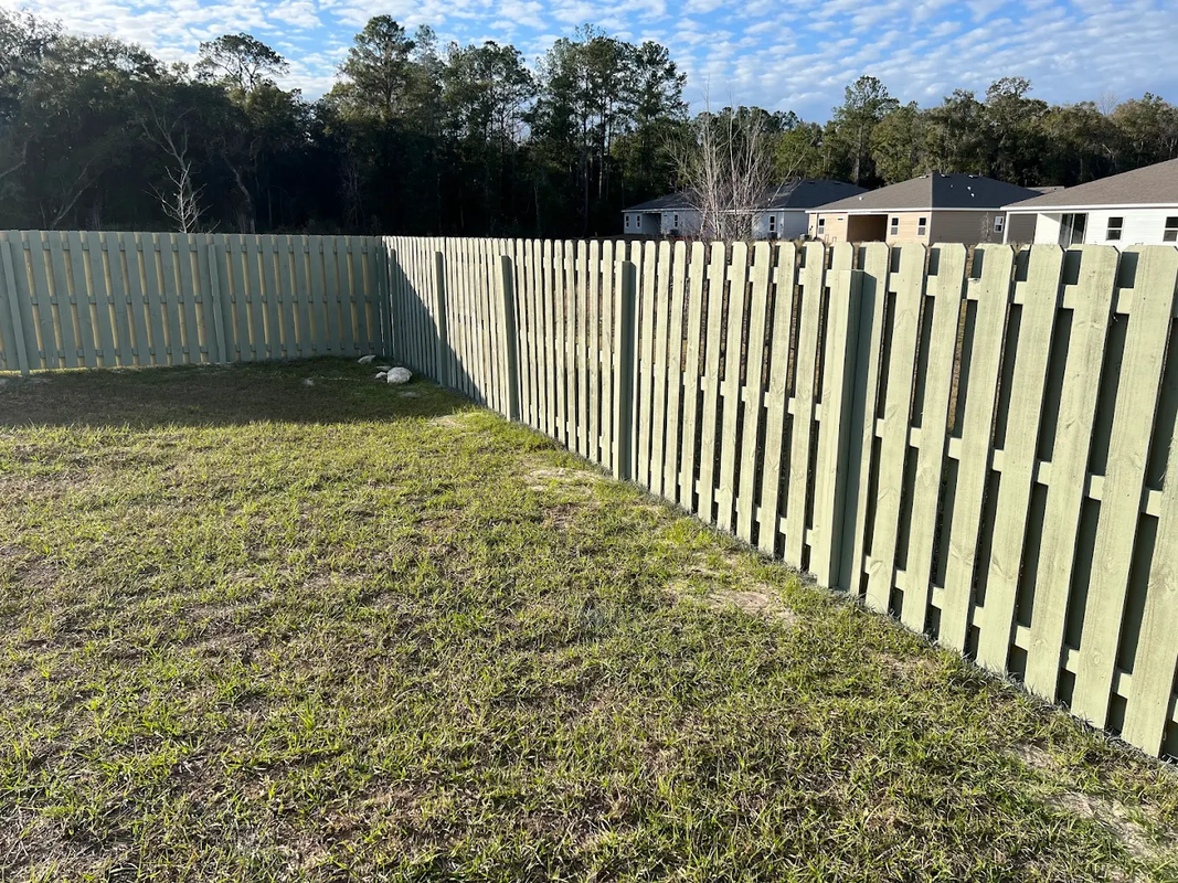 Backyard with a long white wooden fence and grassy yard in sunlight