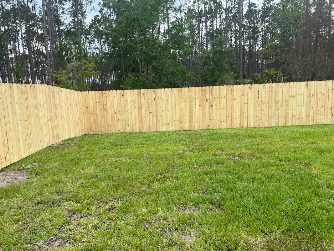 Freshly installed wooden fence enclosing a grassy backyard with trees beyond it
