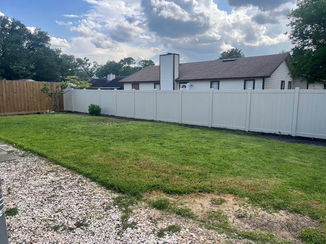 Suburban backyard with white fence, green lawn, gravel path, and cloudy sky