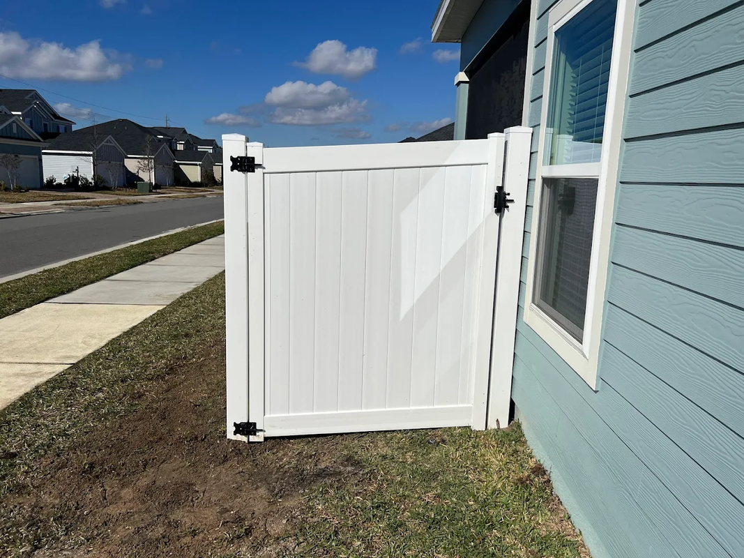 White side gate beside a light blue house along a suburban sidewalk on a sunny day