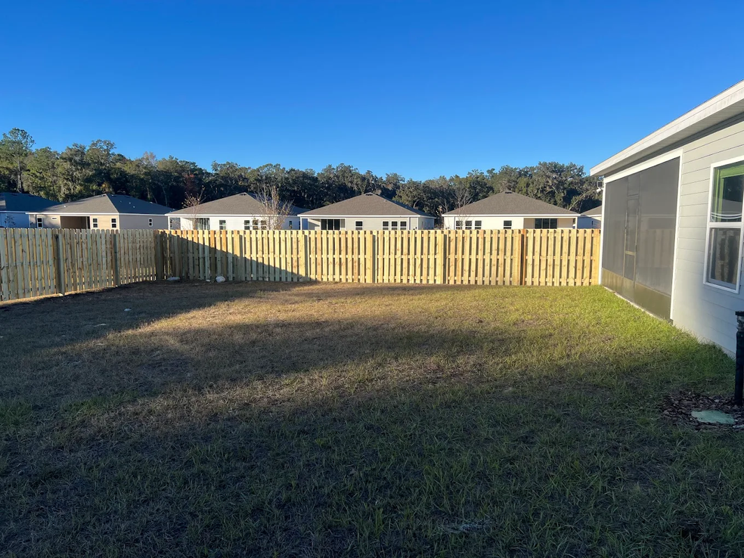 Backyard with wooden fence, grass lawn, and a white house wall in sunlight