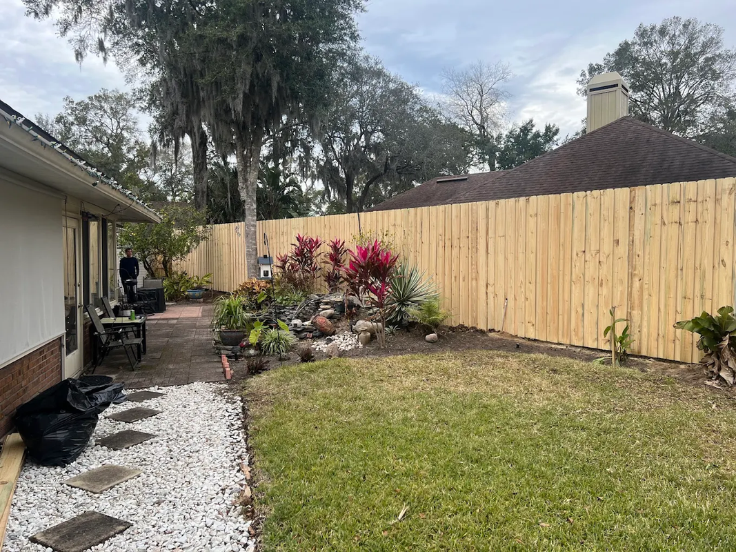 Backyard with green lawn, rock garden, wooden privacy fence, and house side walkway
