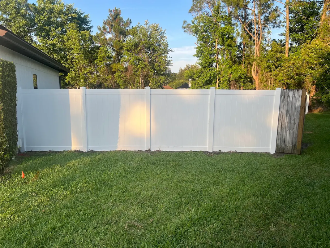 White fence panels in a grassy backyard beside a house, with trees in the background.