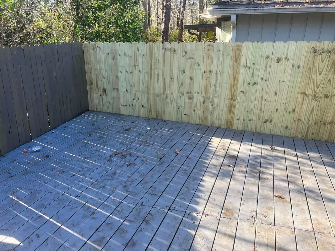 Empty fenced backyard deck with weathered wood boards and green privacy fence.