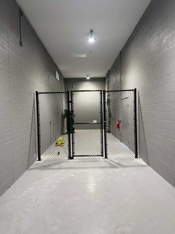 Small fenced indoor kennel with gray walls, white floor, and overhead lights.