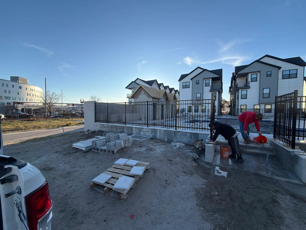 Workers at a construction site beside new houses, with one person bending near a fence in snowy daylight.