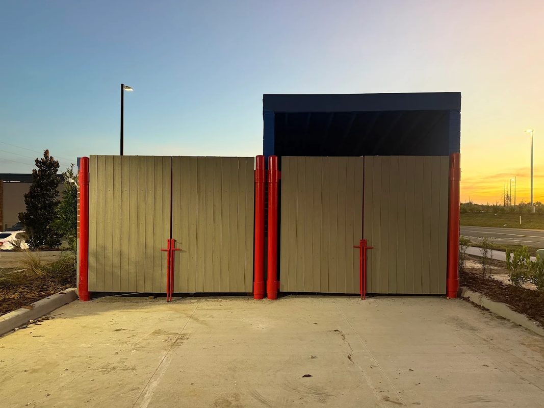 Two tan metal barriers with red posts blocking a paved lane at sunset