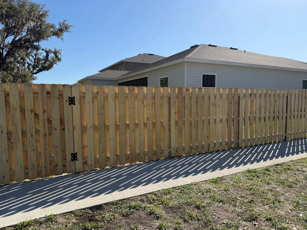 Wooden privacy fence beside a house and sloped concrete driveway under a clear sky