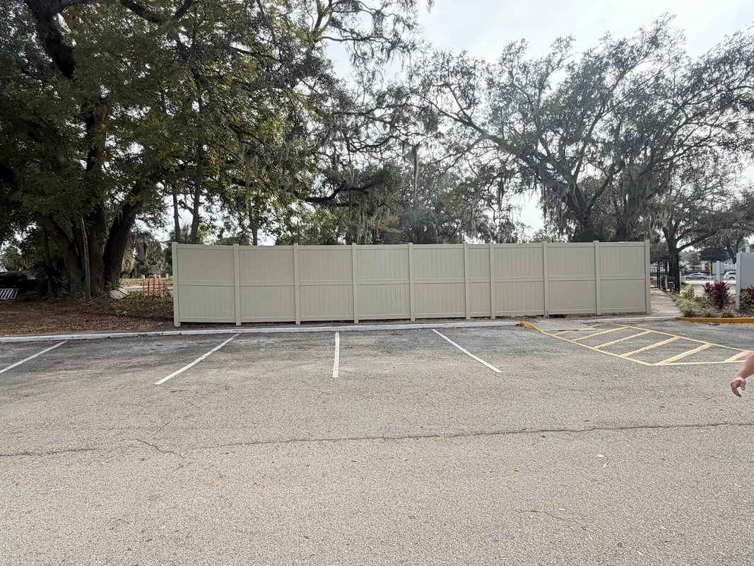 Empty parking lot with white-striped spaces and a beige fence along the back