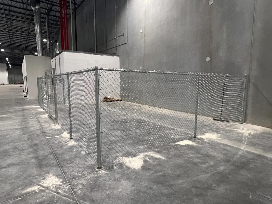 Chain-link fenced-off area inside a large industrial concrete room with white dust on the floor.