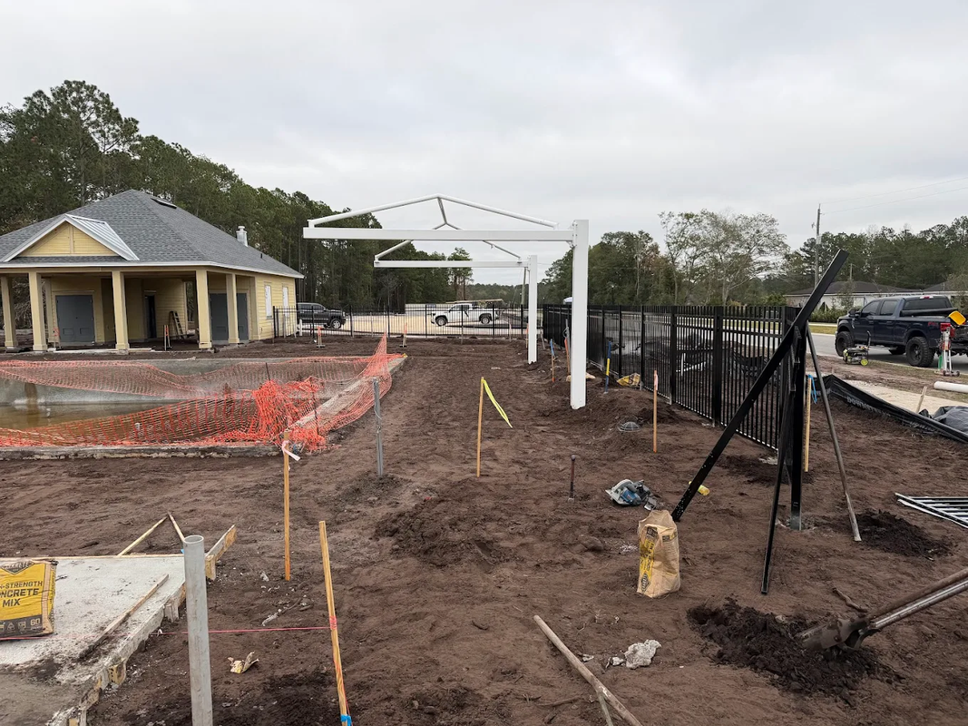 Construction site with a white gazebo, muddy ground, fencing, and a house in the background