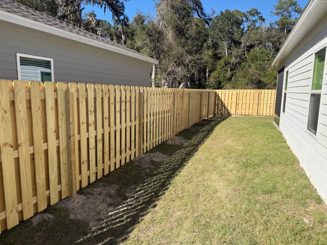 Wooden privacy fence beside a narrow grassy side yard between two houses on a sunny day