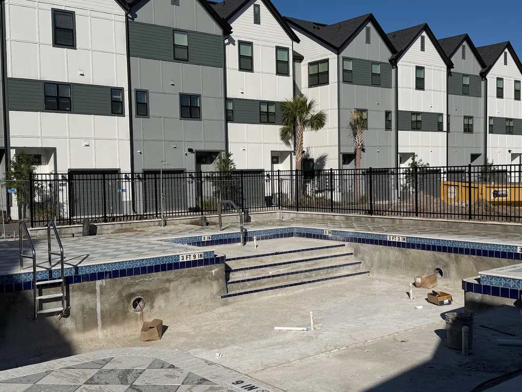 Empty drained pool with steps and scattered debris beside apartment buildings.