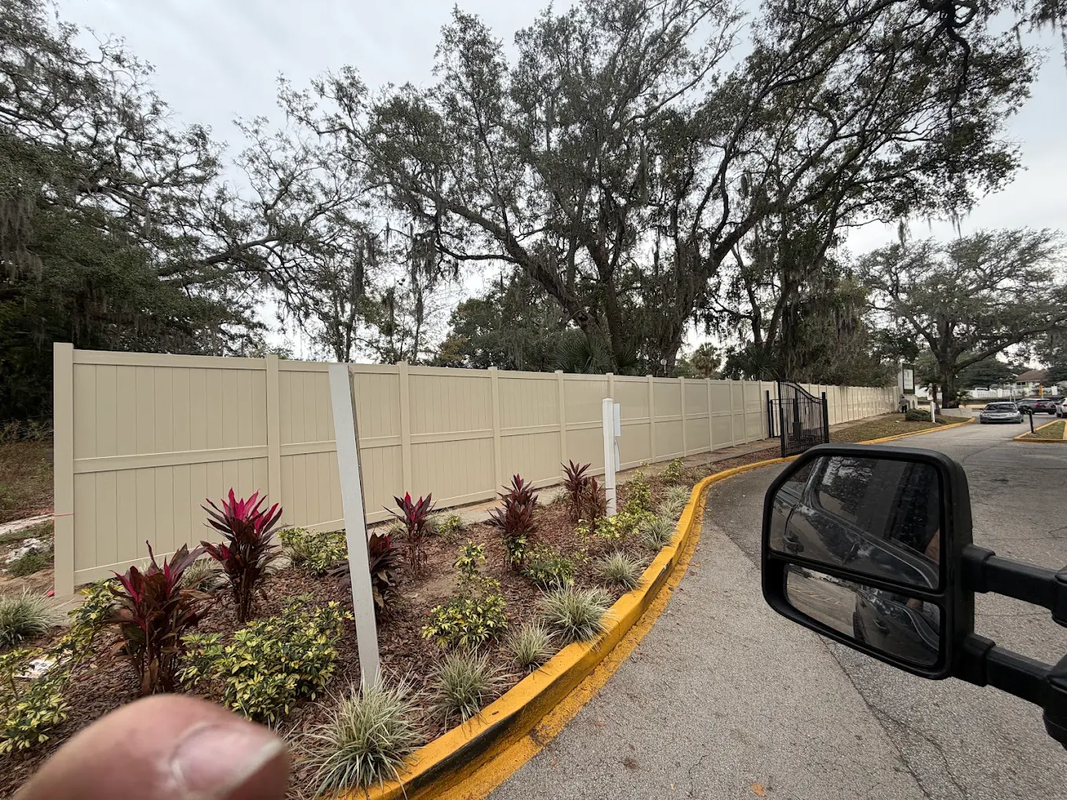 Curved beige wall with red shrubs along a road beside a car mirror and trees