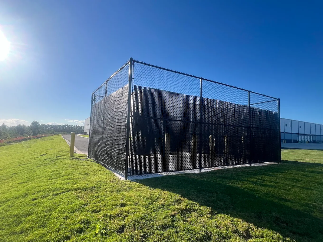 Black mesh-covered structure on a grassy field under bright blue sky