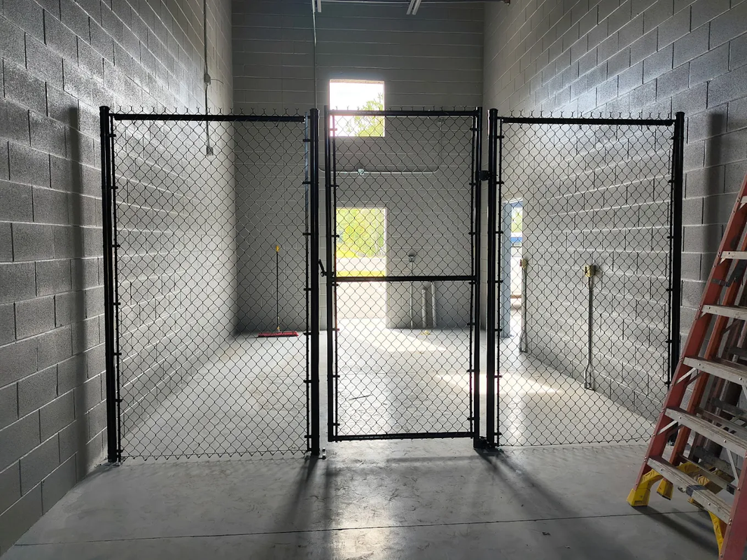 Empty industrial room with cinderblock walls, black metal fencing, and a ladder on the right.