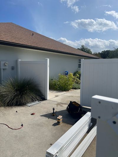 Backyard patio with white fence panels, potted plants, and stacked white trim boards on concrete.