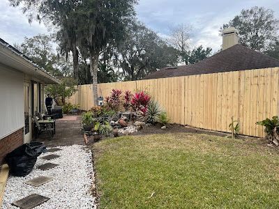 Backyard with green lawn, rock garden, wooden fence, and house walkway on the left.