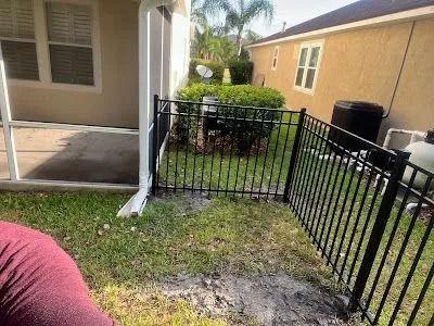 Backyard patio with black metal fence, grass patch, and beige house exterior.
