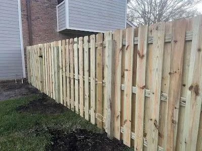 Wooden privacy fence beside a house along a muddy yard