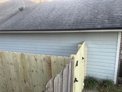 Wooden fence corner beside a gray house exterior and roofline.
