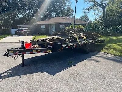 Flatbed trailer carrying stacked camouflage gear parked on a suburban street in front of a house.