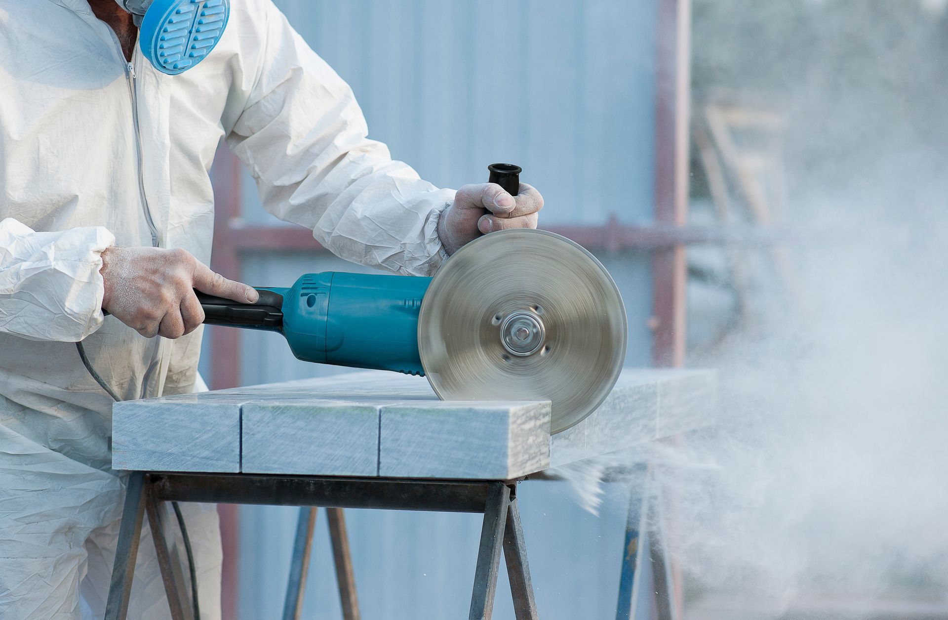 Person wearing protective gear uses a power grinder to cut stone, creating dust. Person wearing protective gear uses a power grinder to cut stone, creating dust.