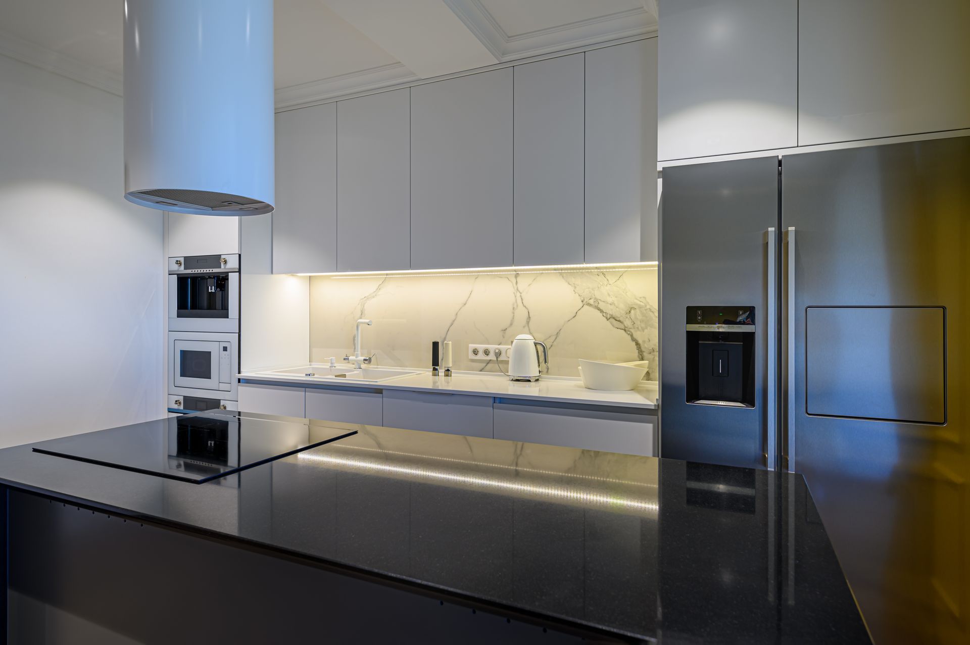 Modern kitchen with white cabinetry, marble backsplash, stainless steel refrigerator, and black island. Modern kitchen with white cabinetry, marble backsplash, stainless steel refrigerator, and black island.