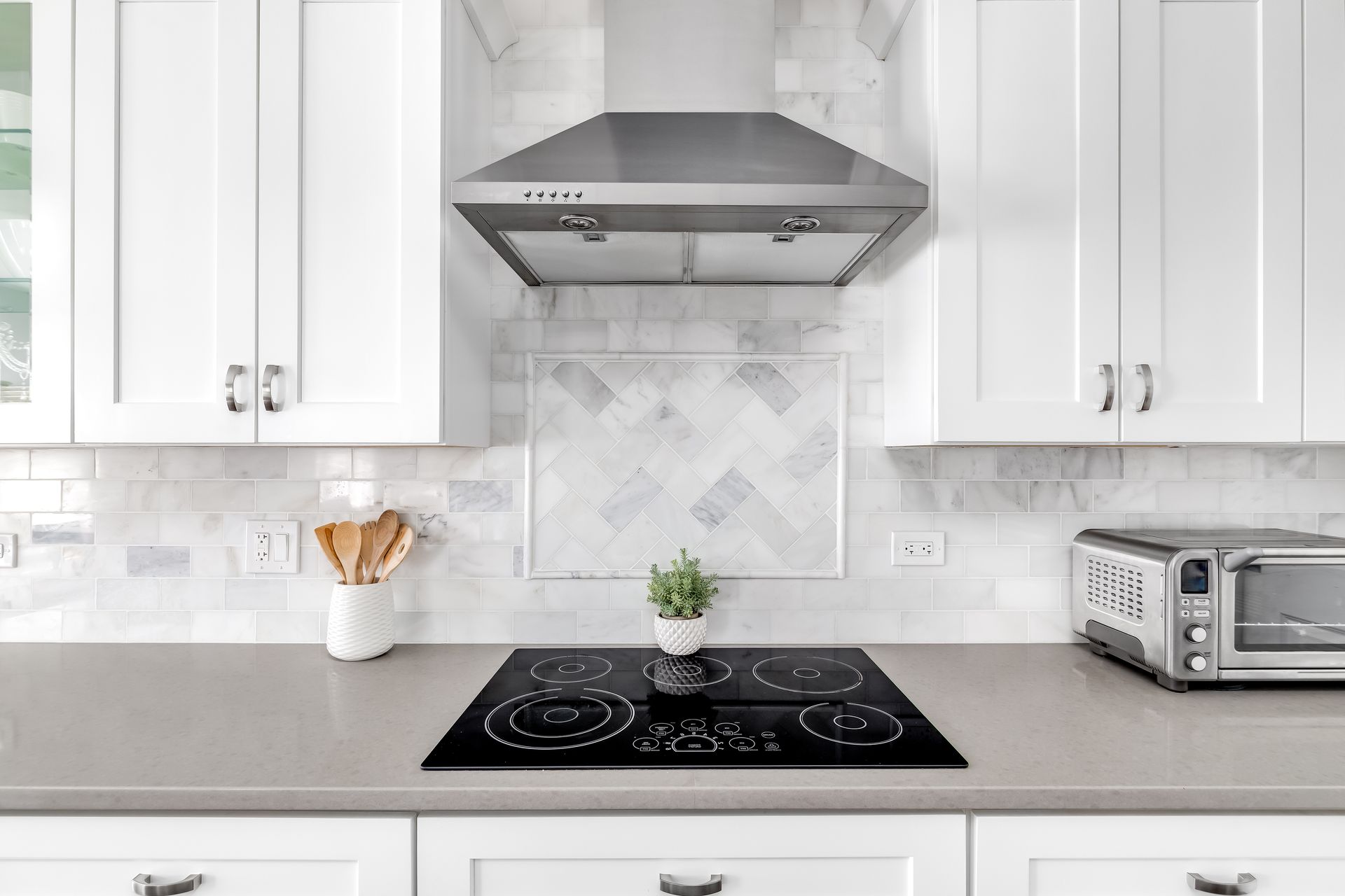 Kitchen with white cabinets, stainless steel range hood, black cooktop, gray countertop, and white backsplash. Kitchen with white cabinets, stainless steel range hood, black cooktop, gray countertop, and white backsplash.