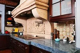 Kitchen with stone range hood, blue countertop, dark cabinets, and tile backsplash.