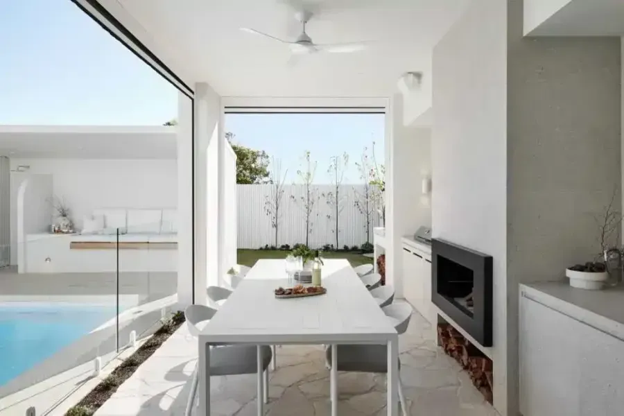 Outdoor dining area with white table, fireplace, and pool view.