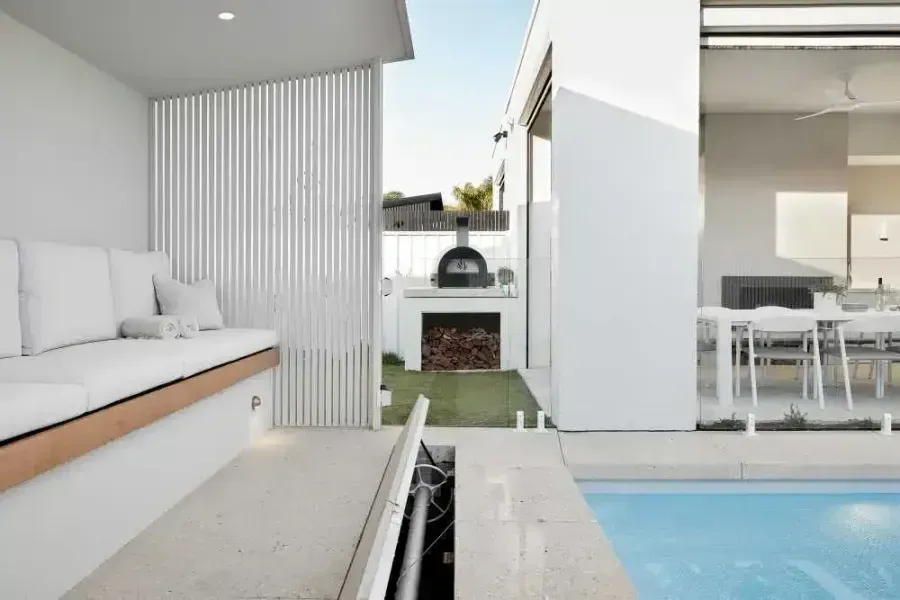 Modern outdoor space with white walls, seating, pool, and pizza oven.