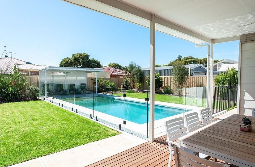 Backyard with a swimming pool, lawn, and deck with outdoor dining table, under a bright blue sky.