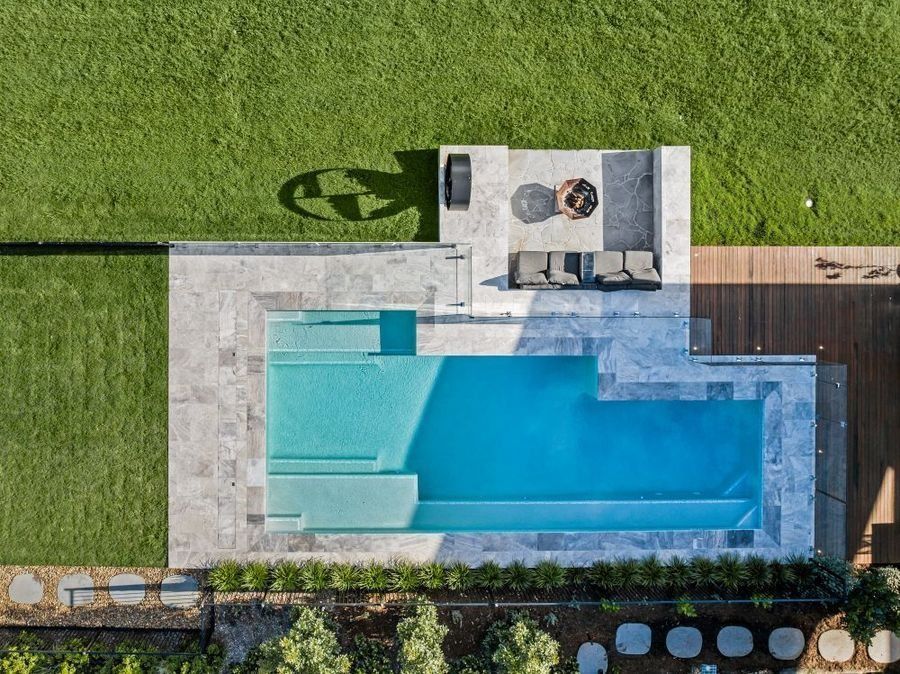 Overhead view of a backyard with a blue rectangular pool, patio, lawn, and outdoor seating around a fire pit.