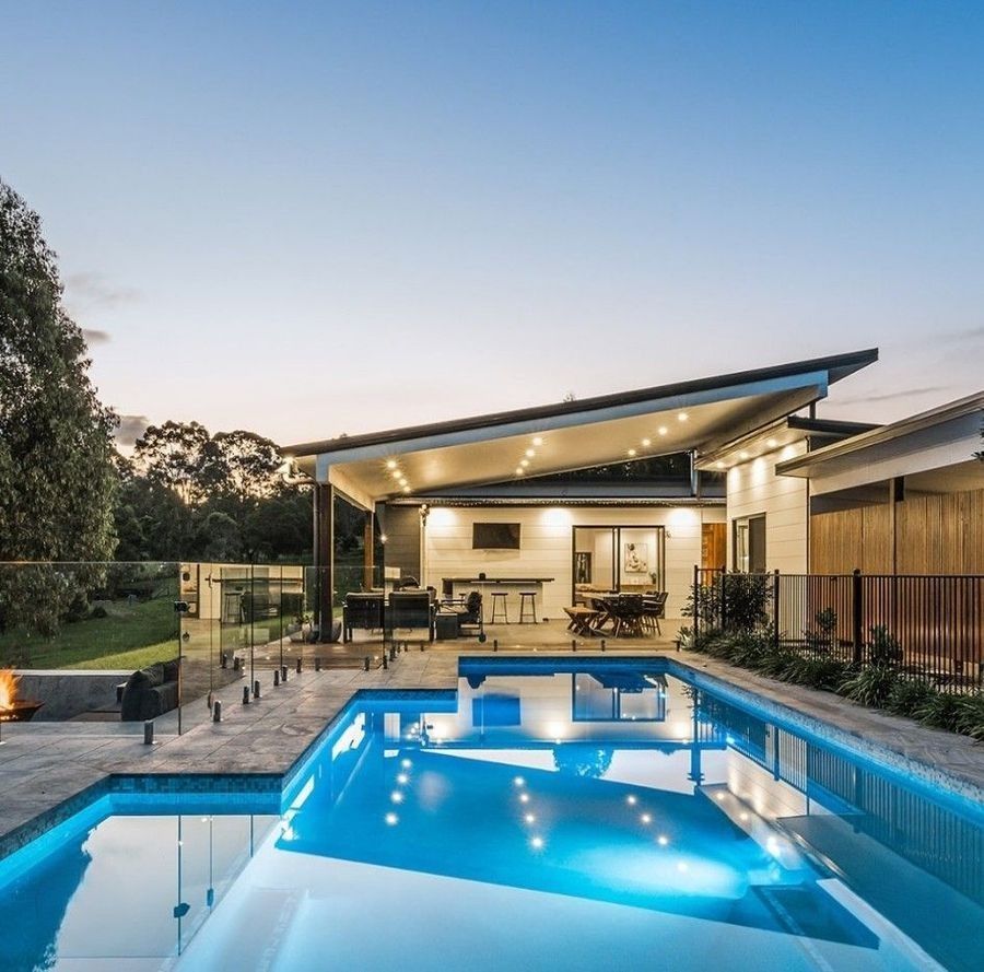 Modern house with pool at dusk, lit pool water, patio, outdoor seating.