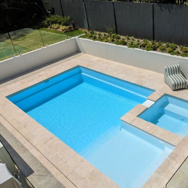 A rectangular swimming pool with attached spa and a striped chair, surrounded by a white wall.