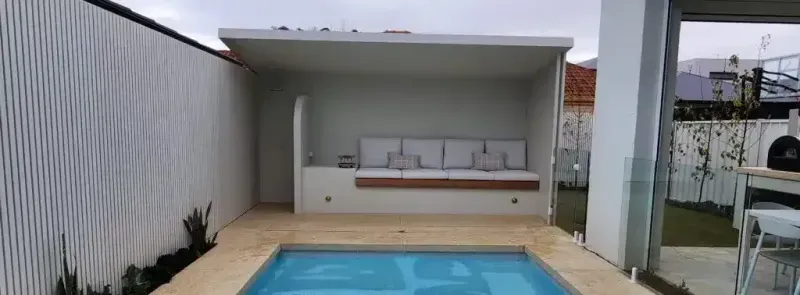 Backyard with a small pool, patio seating area, and white vertical slatted wall.