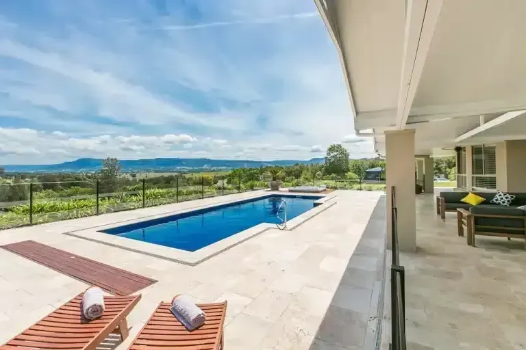 Pool with lounge chairs and scenic view under a bright blue sky.