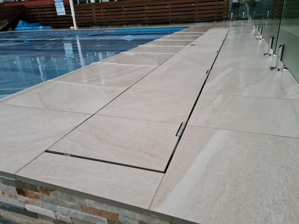 Poolside with tiled deck, a shallow gutter, and glass fencing. Pool has a blue cover.
