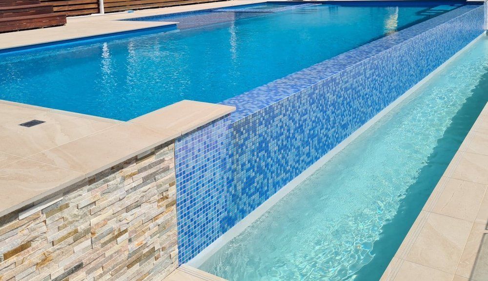 Swimming pool with blue tiles and cascading water into a surrounding trough.