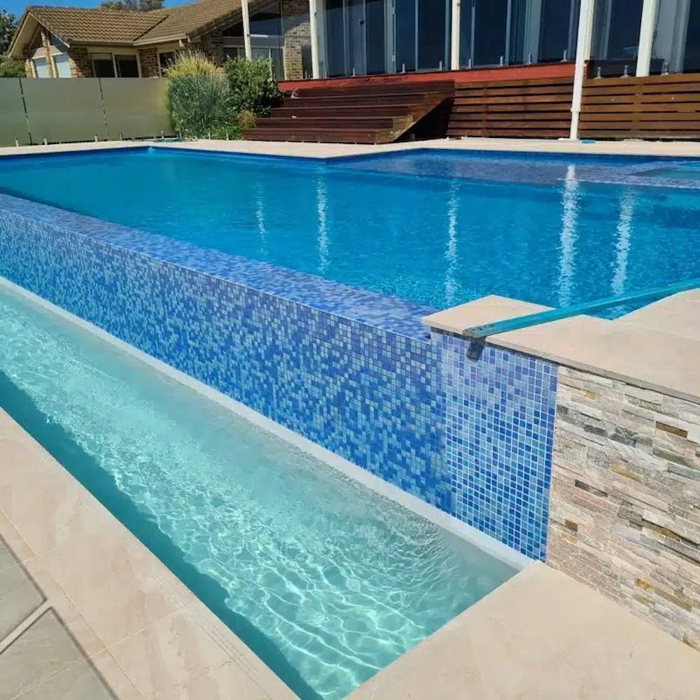 Blue tiled pool with a long overflow gutter, set against a house with a wooden deck.