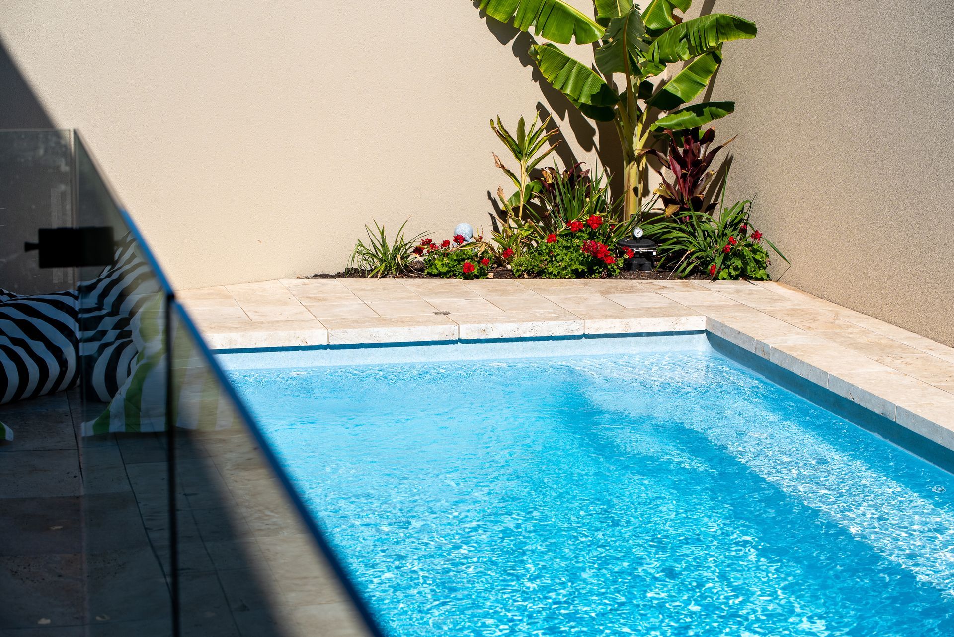 Overhead view of a rectangular turquoise pool, pergola, and green lawn.