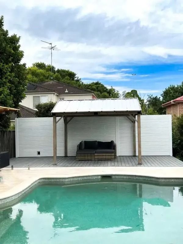 Swimming pool with shaded lounge area, white fence, and cloudy sky.