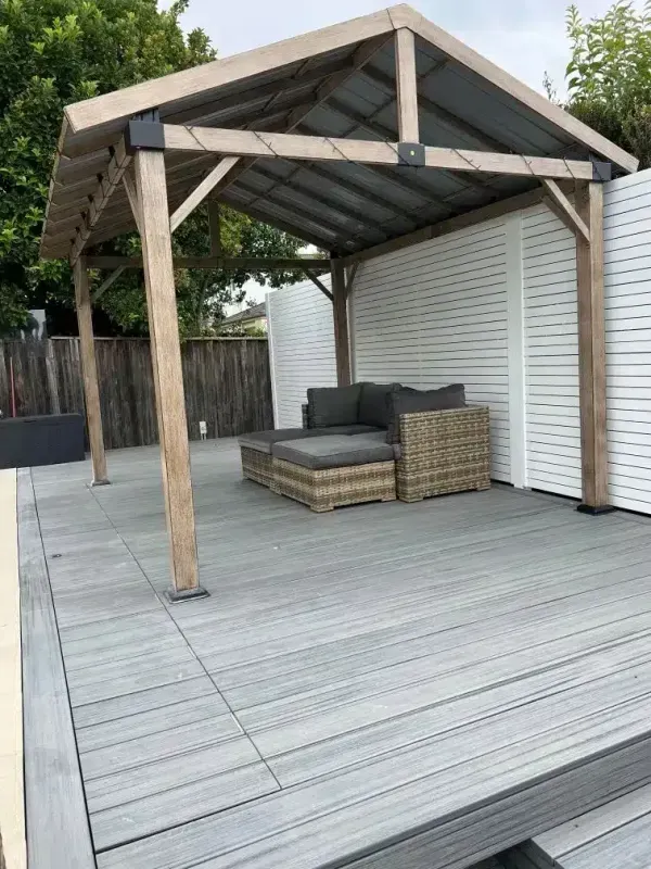Outdoor seating area with grey composite decking, a wooden pergola, and a wicker sofa.